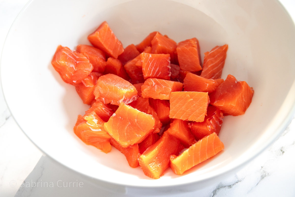 Bright red-orange cubes of salmon in a white bowl.