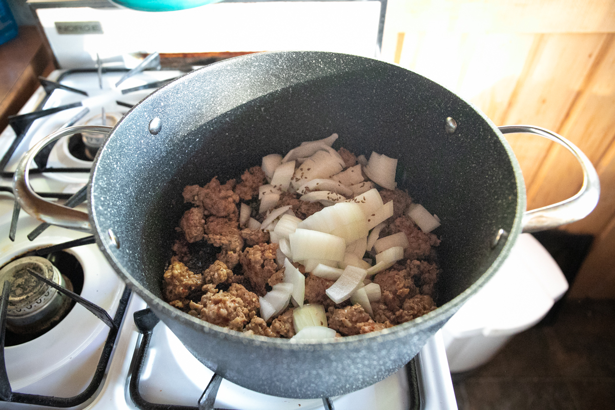The black pot with sausage has chopped white onions on top.