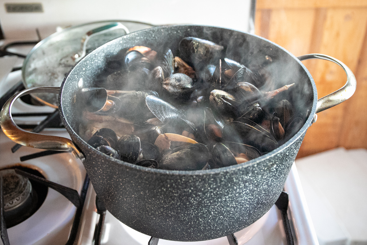 Steam rising fro a large black pot filled with black mussels.