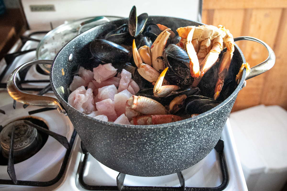 White cubes of fish are added to the pot beside crab and mussels. 