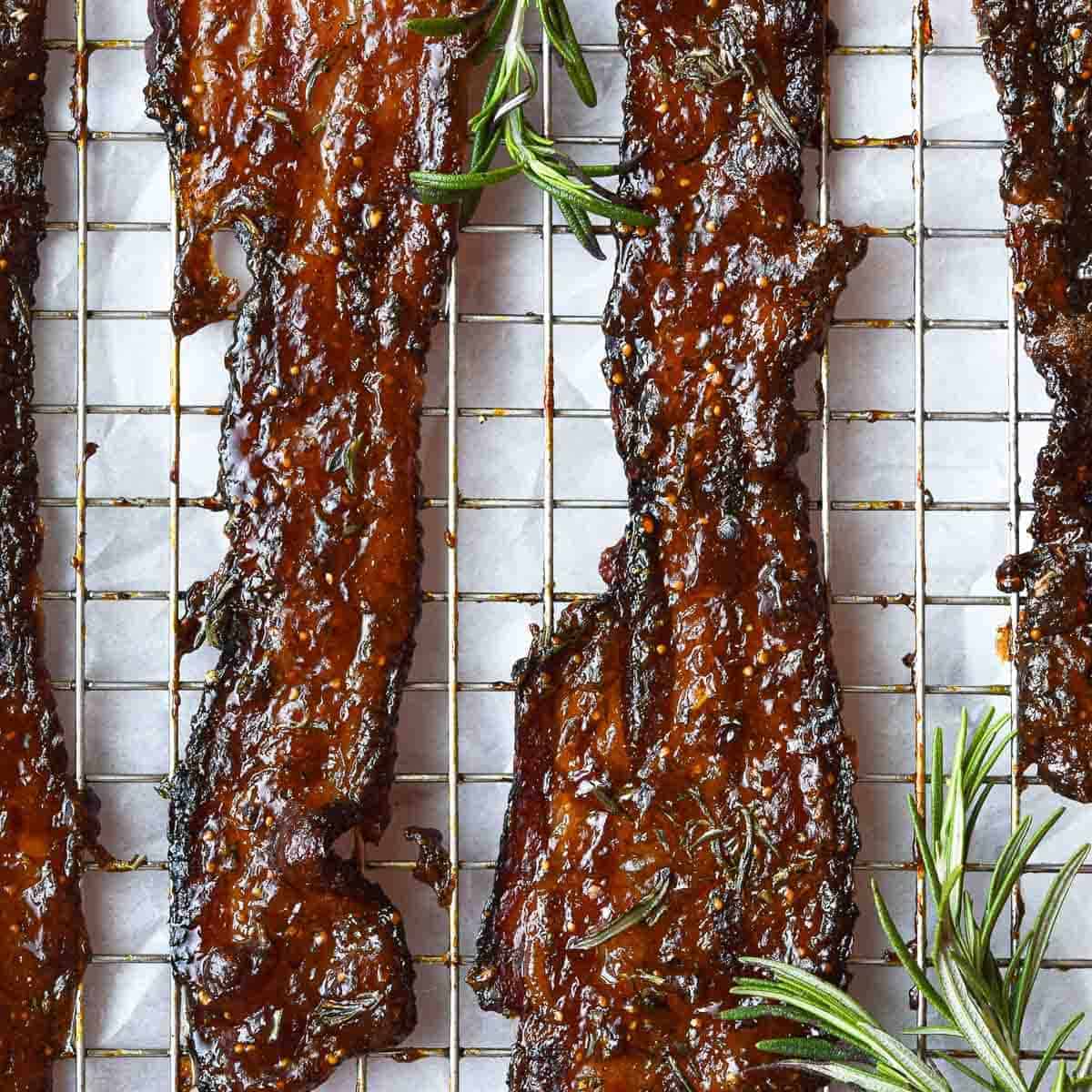 Strips of caramelized bacon on a cooling rack with sprigs of rosemary around.