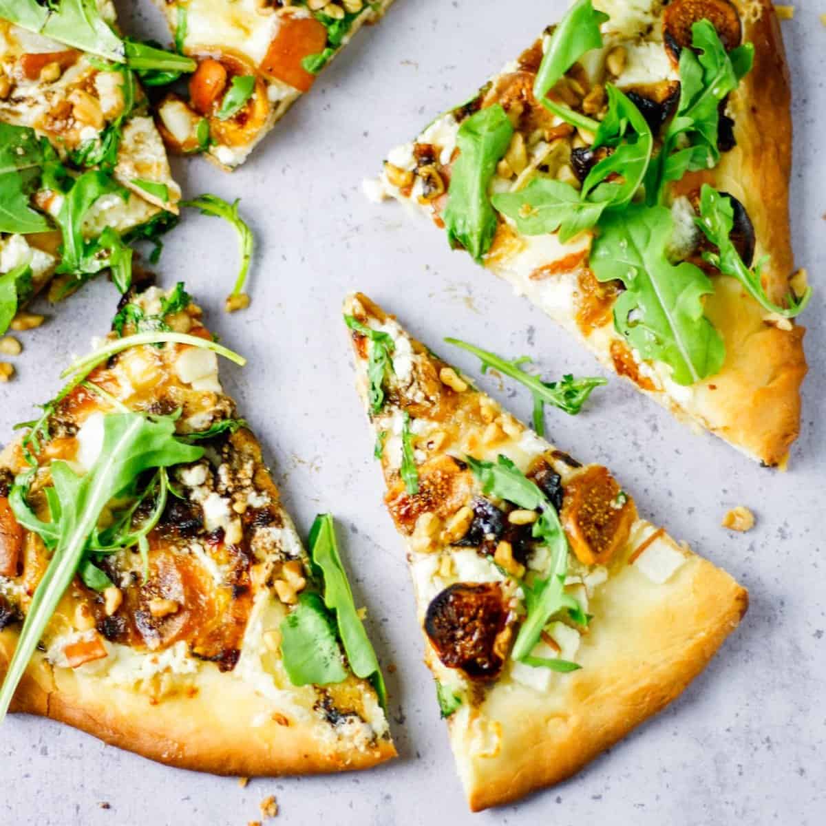 Pizza cut into wedges and topped with fig quarters, walnuts, brie cheese and fresh arugula.