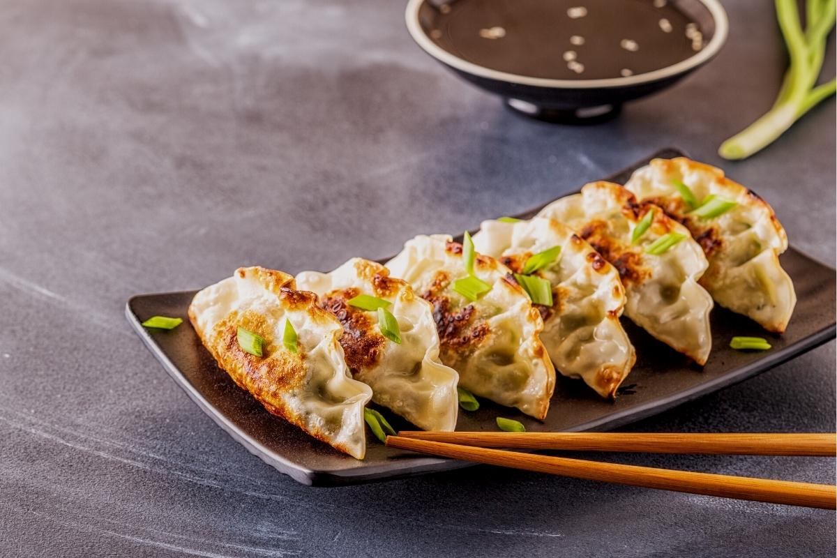 A row of 6 pan-fried gyoza dumplings on a black rectangular plate.