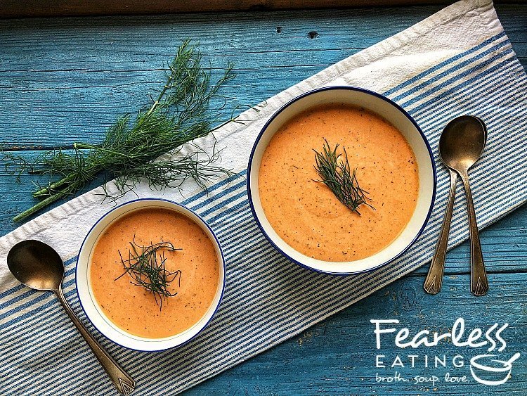 Creamy orange colored salmon bisque in blue and white bowls with fresh dill fronds alongside.