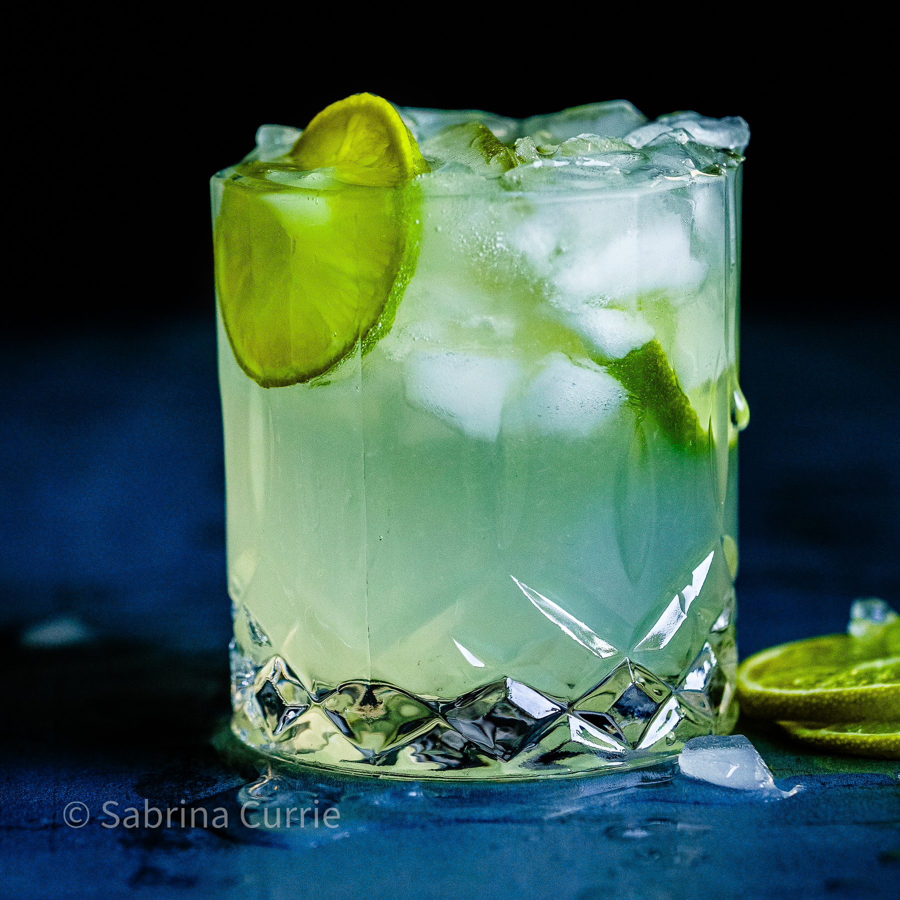 A vodka gimlet with lime in a rocks glass with a dark blue background