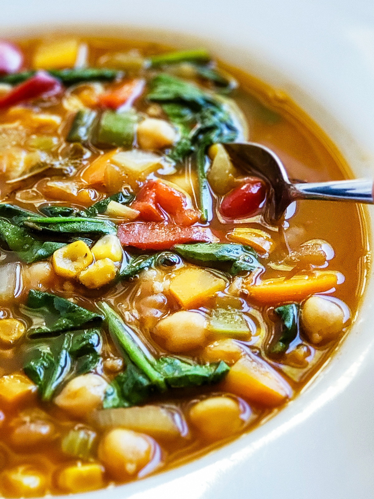 Close up of the vegetable soup full of corn kernels, green spinach, carrots and celery.