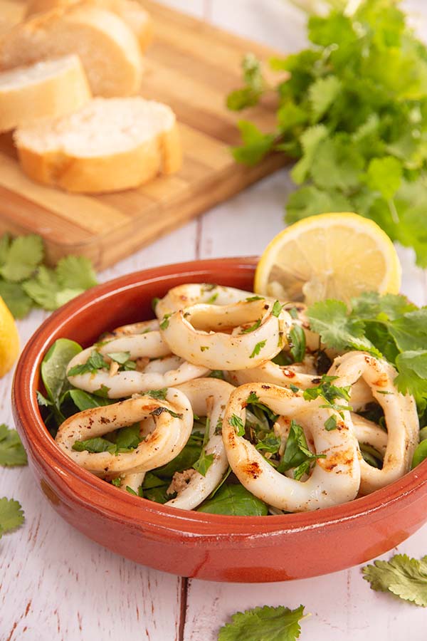 Round white calamari rings in a terracotta colored bowl with lettuce and lemon wedges.