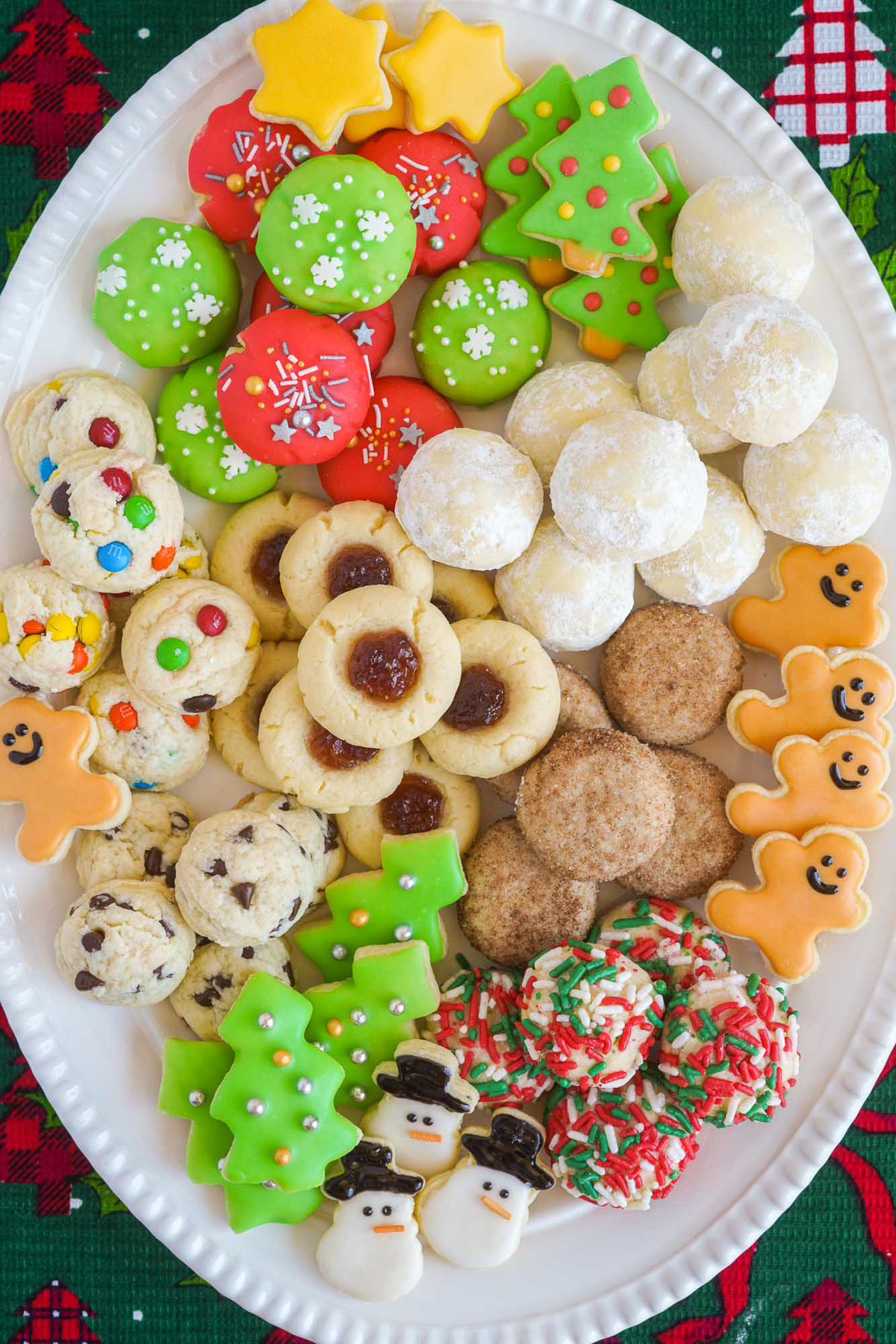 A large white oval platter with 8 kinds of assorted, Christmas decorated cookies in shades of white, red and green.
