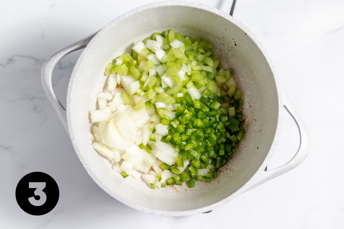 White pot with diced celery, green bell pepper and onion in it.