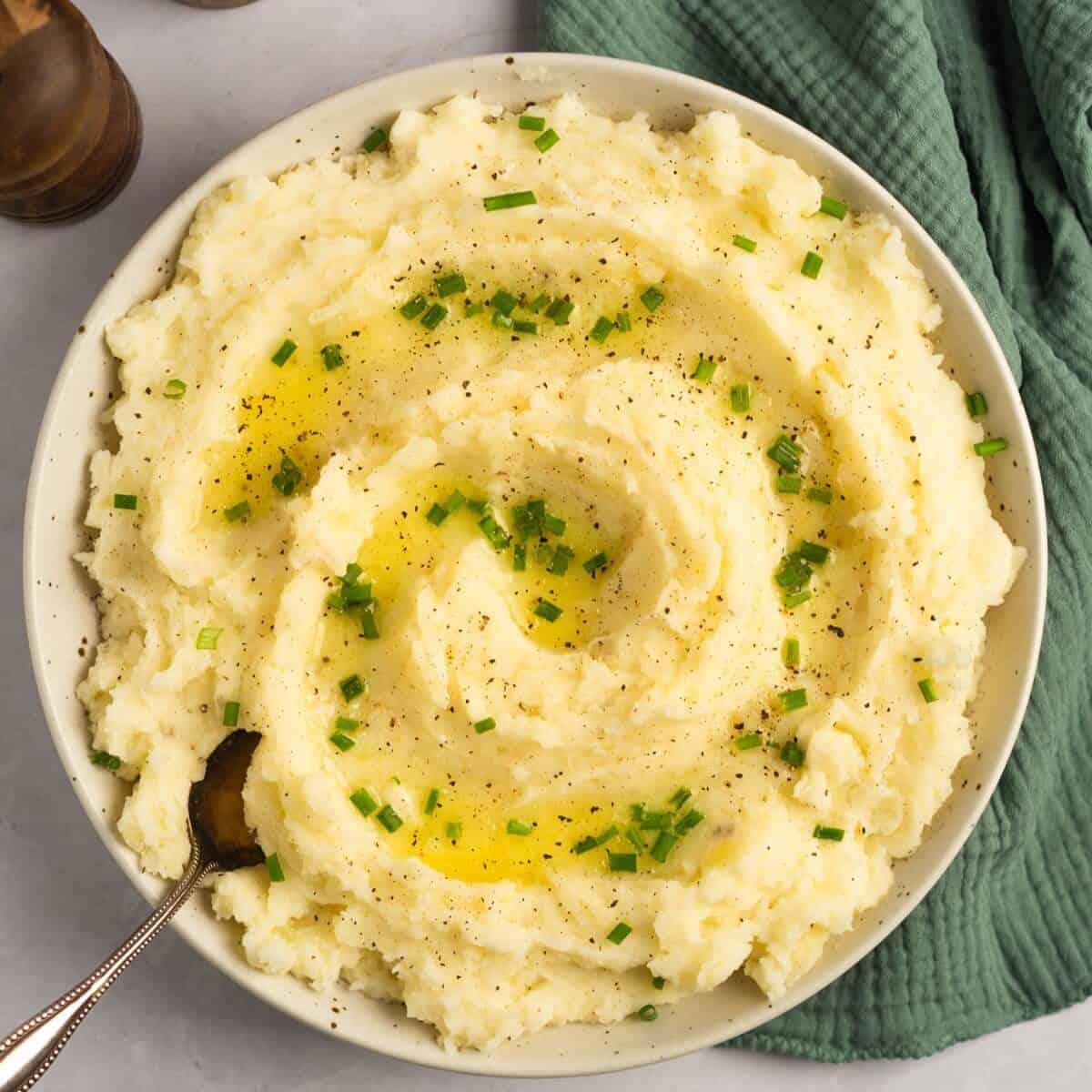 Creamy white mashed potatoes sprinkled with finely chopped green parsley in a white bowl.