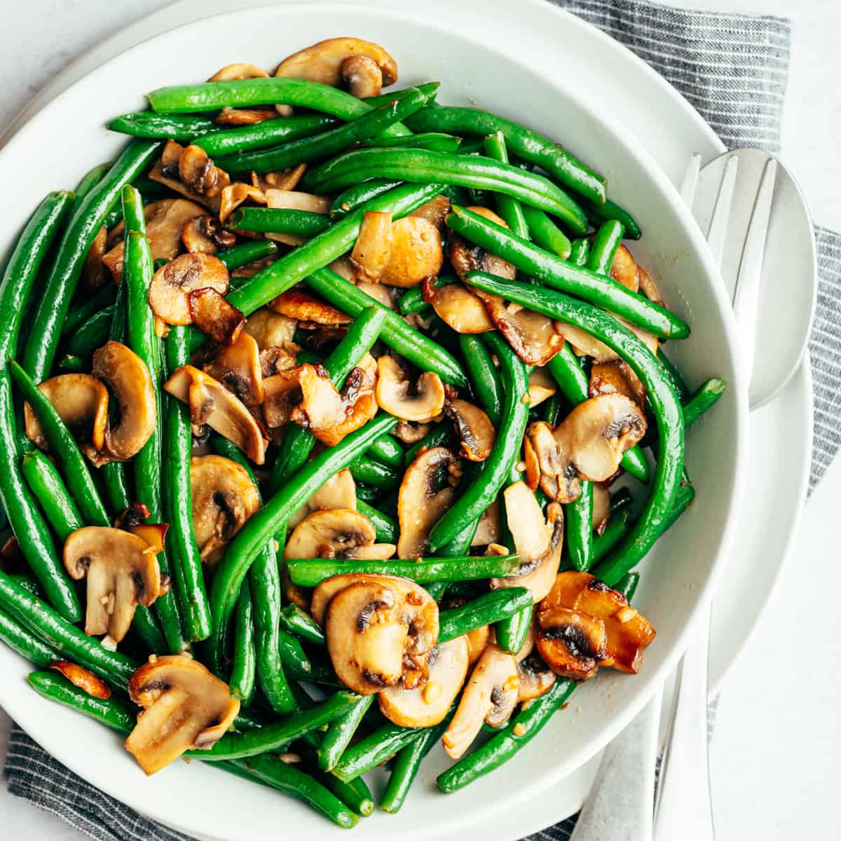 Bright green bean salad with sliced mushrooms all in a white bowl.