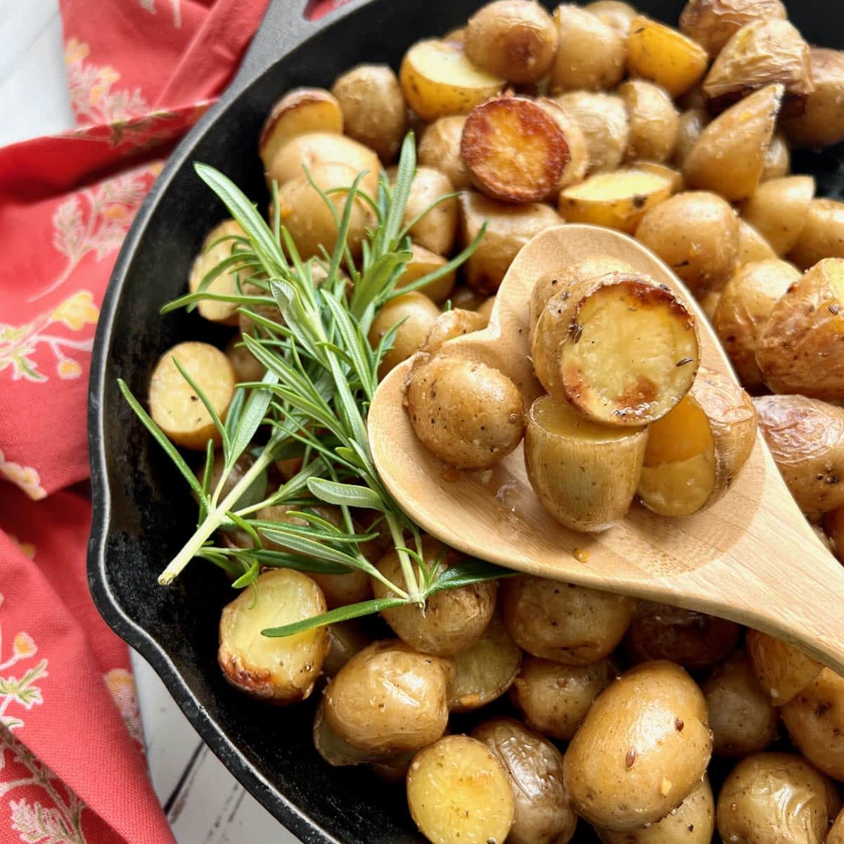 Roasted, halved new potatoes in a black pan garnished with fresh green rosemary sprigs.