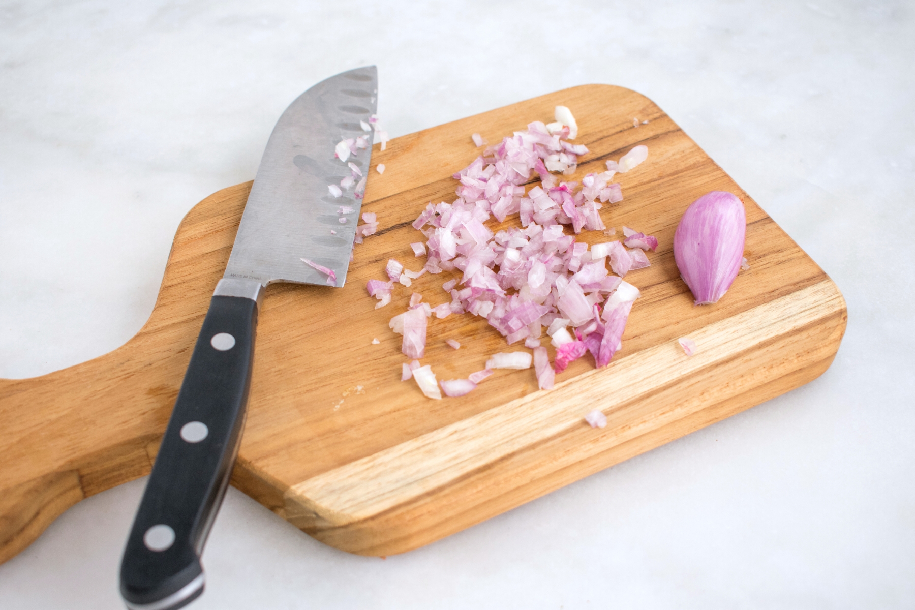 Finely chopped shallots on a wooden cutting board with knife beside.