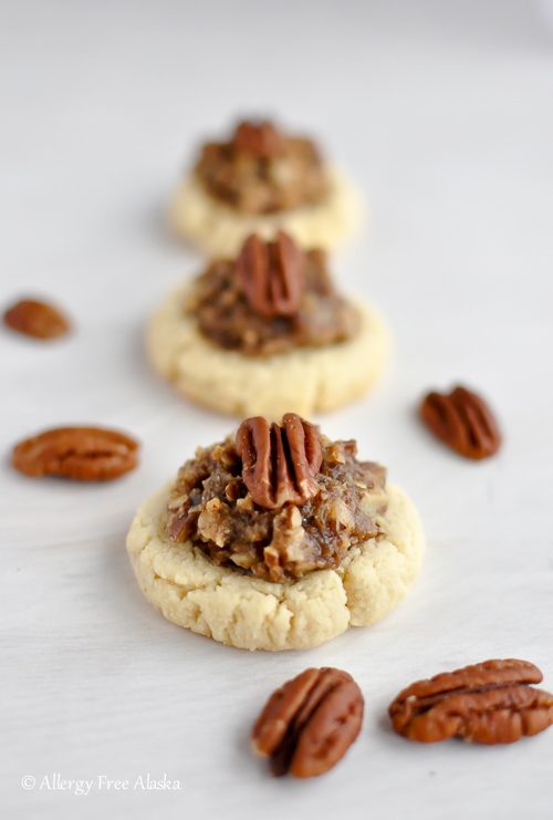 Pecan filled white cookies with pecans scattered around on the white table.