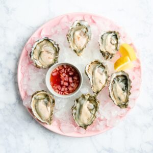 Round pink plate with shucked oysters, a lemon wedge and bright pink oyster vinaigrette.