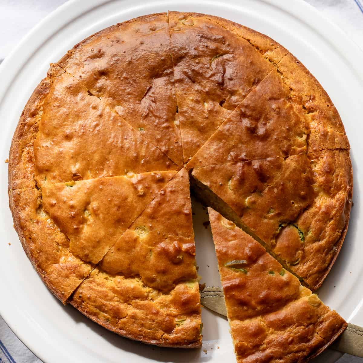 A round loaf of golden cornbread with one wedge cut and partway out of the loaf.