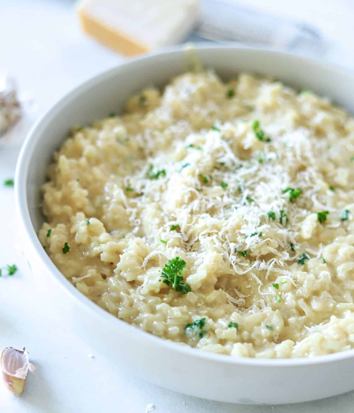 White bowl with creamy white risotto topped with shredded Parmesan cheese and finely chopped parsely.