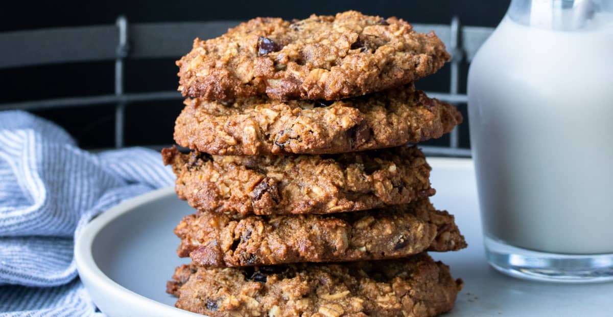 A stack of 5 oatmeal raisin cookies on a plate with milk and a cloth napkin beside.