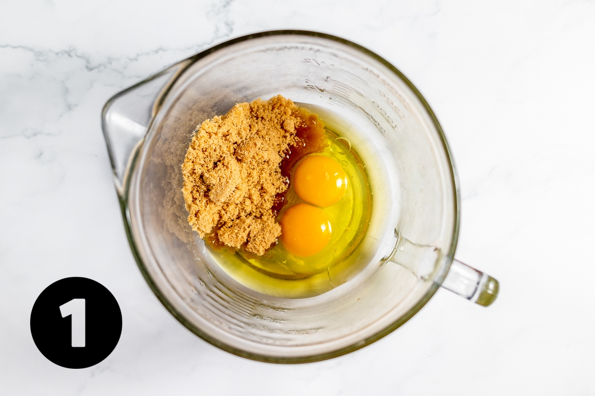 Large glass measuring cup with 2 eggs and brown sugar in it.