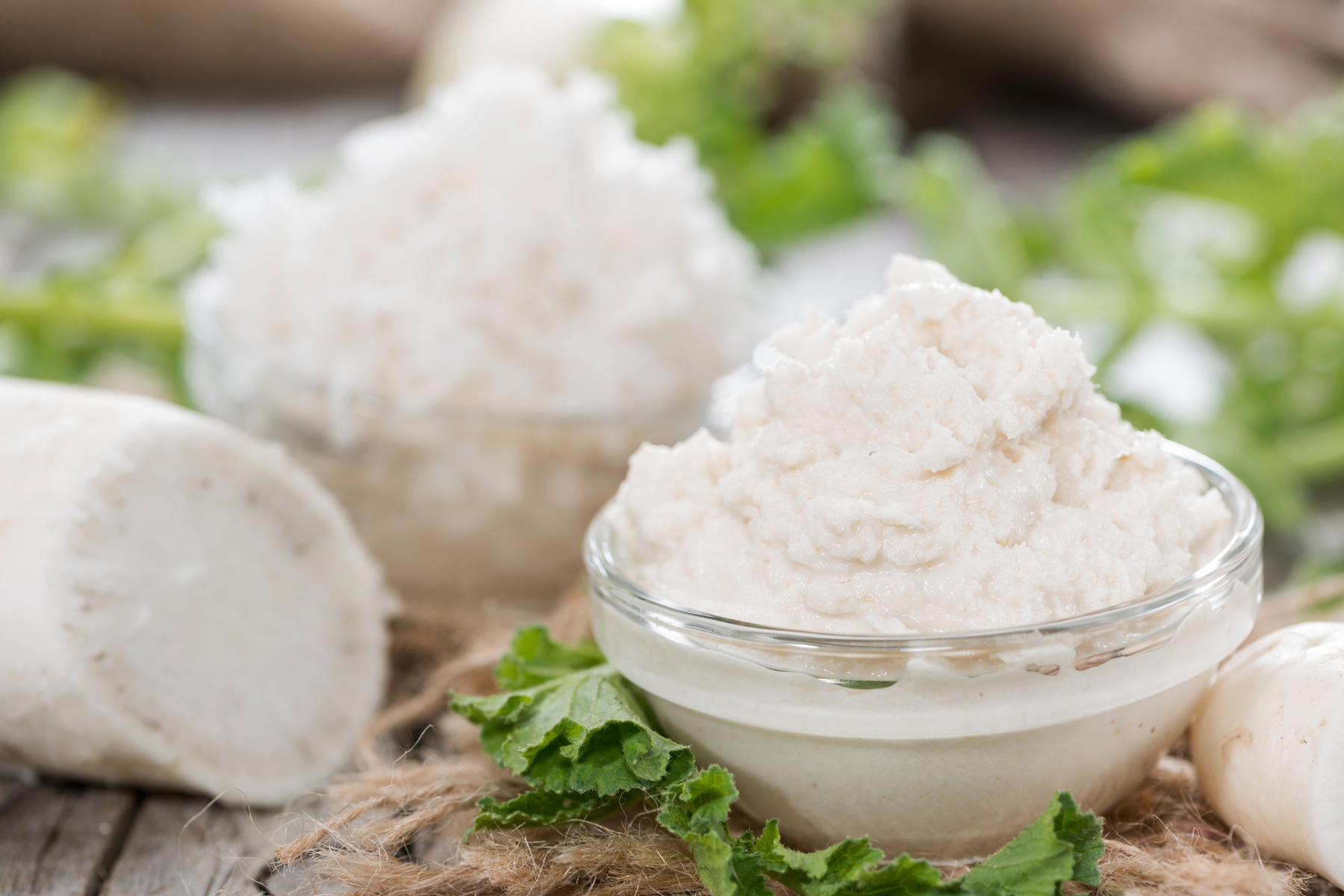 Creamed white horseradish in a small glass dish with greens in the background.