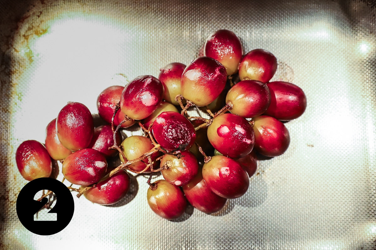 A large bunch of roasted and slightly wrinkled red grapes in a steel pan.