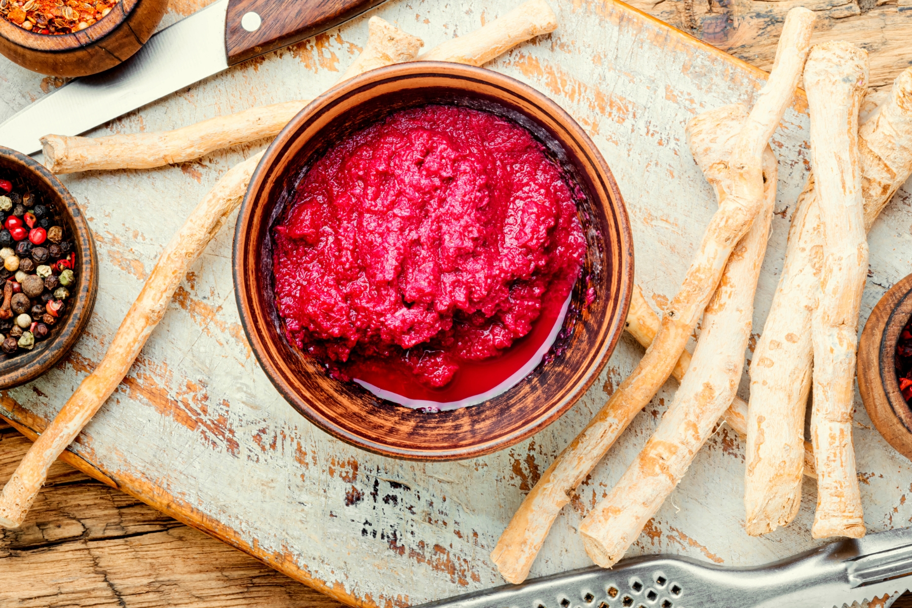 Bright pink-red beet horseradish sauce in a pottery bowl with peeled horseradish roots beside.