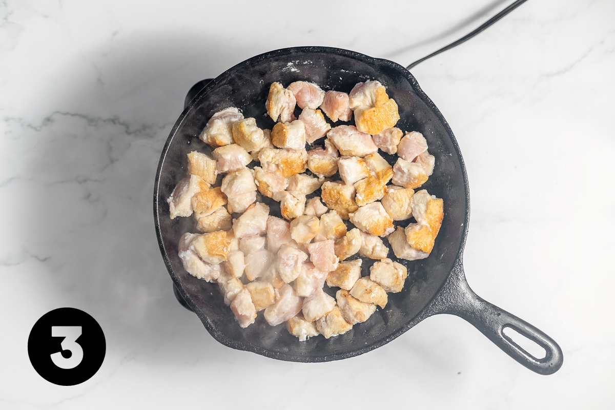 Chicken cubes being fried in a black, cast iron pan.