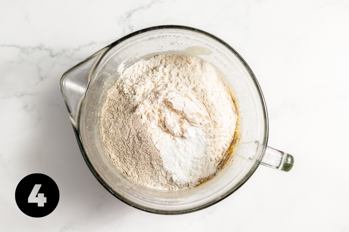 The two types of flour and other dry ingredients have been dumped into the glass bowl on top of the wet ingredients.