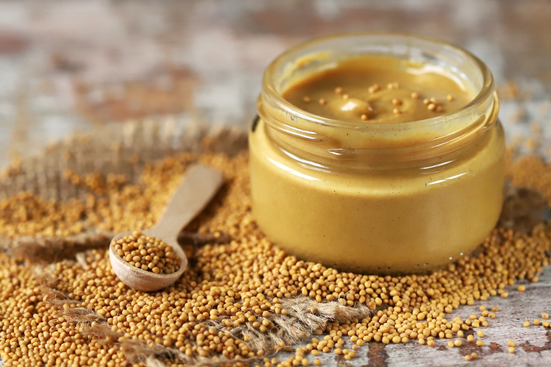 Jar of brown mustard with light brown mustard seeds all around the bottom of the jar.