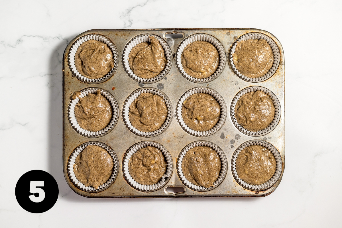 Medium brown colored batter is in 12 paper muffin cups in a metal muffin tin.