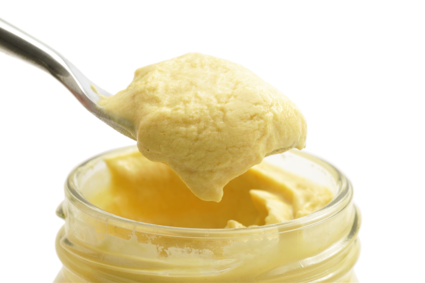 Creamy pale yellow Dijon mustard being scooped out of a jar with a spoon.