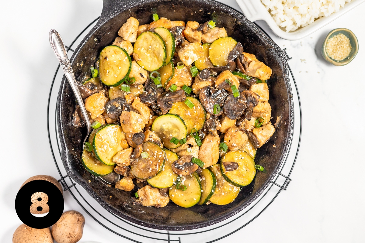 Cooked golden chicken pieces are added back to the pan with zucchini, mushrooms and sauce for a stirfy with a deep brown glazed look.