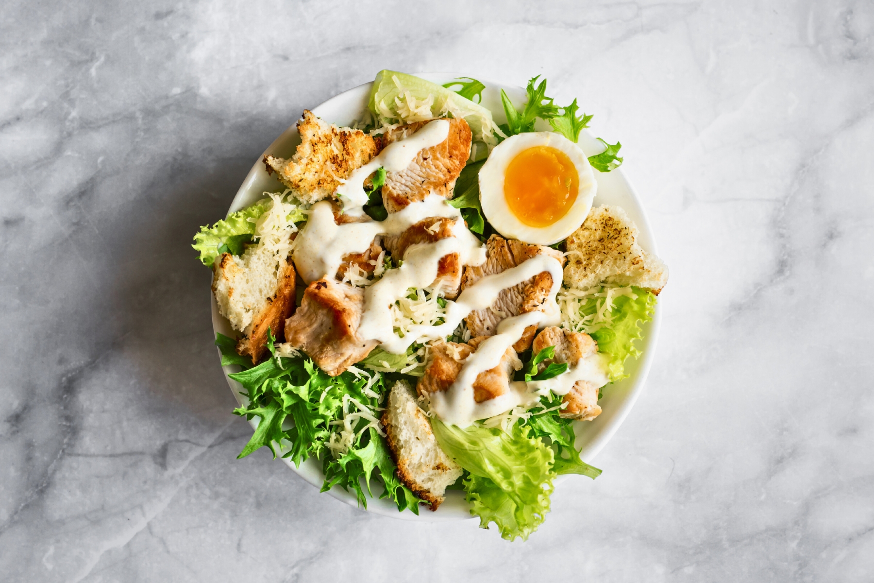 Green salad topped with chunky croutons, half a soft boiled egg and a drizzle of creamy white dressing over top.