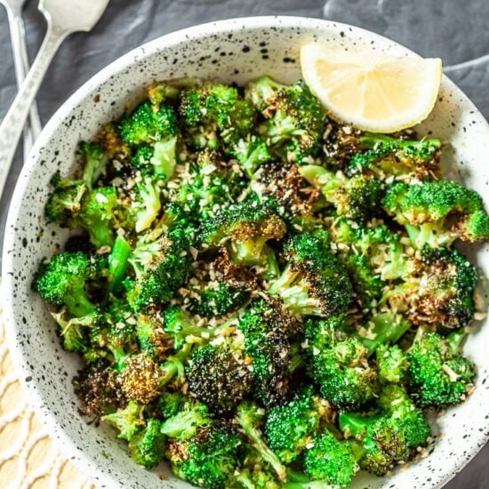 Bright green roasted broccoli florets with dark brown spots in a black and white speckled bowl.