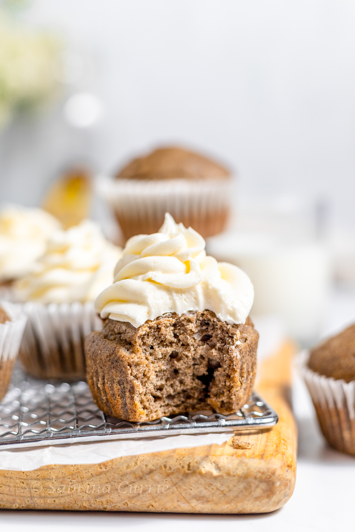 Closeup of a tender brown muffin with creamy white frosting on top and a big bite out of the front.