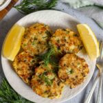 Herb flecked fish cakes on a plate with lemon wedges.