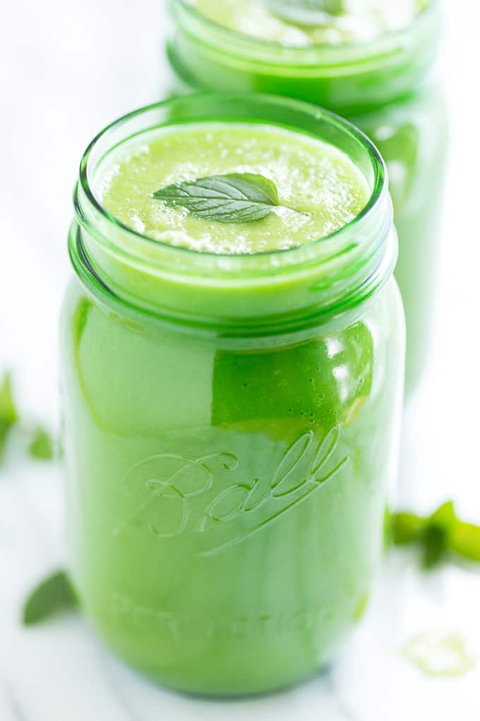 Bright green smoothie in a canning jar glass with a mint leaf on top.