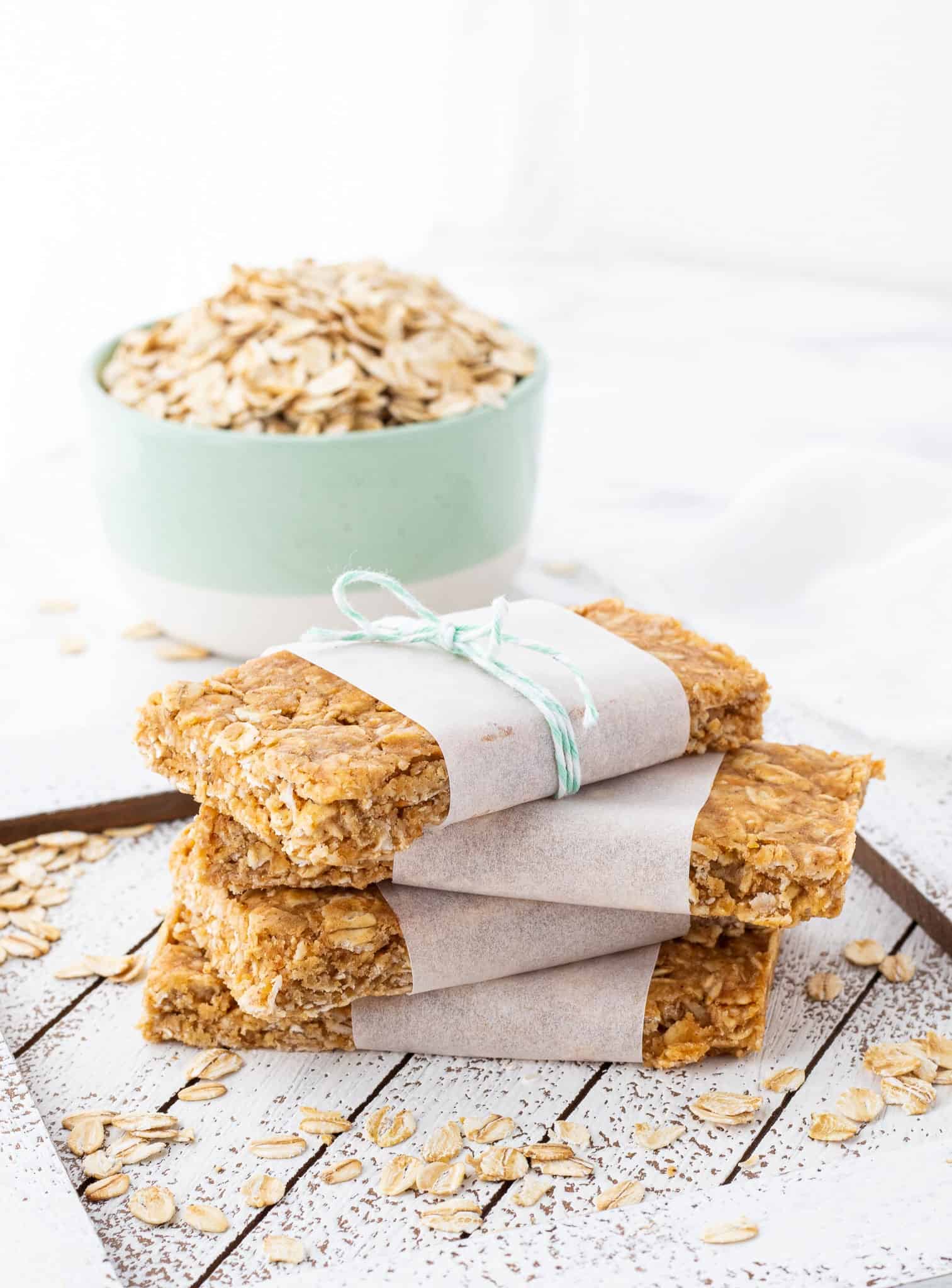 A stack of 4 parchment wrapped oat bars with a bowl of oats in the background.