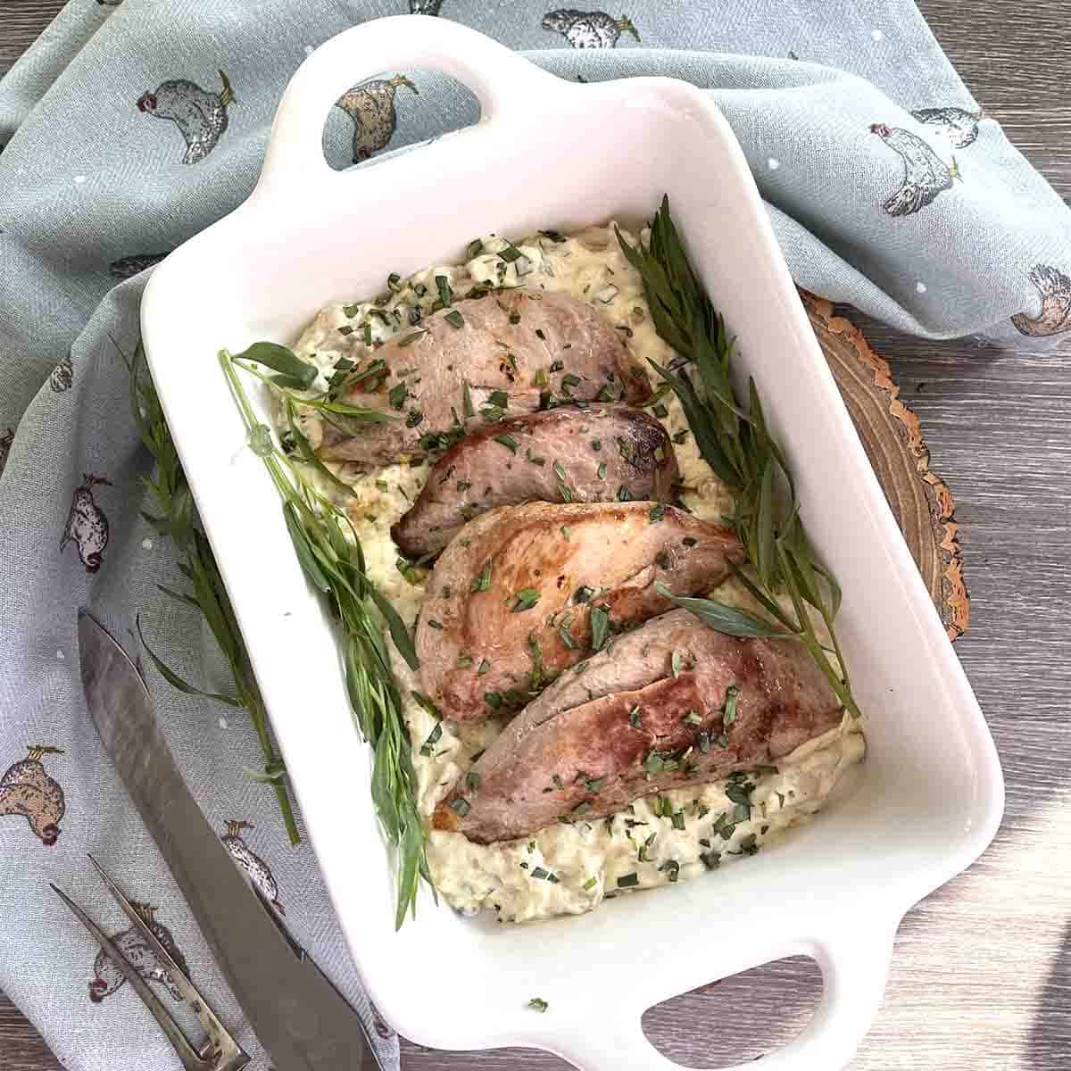 White rectangular casserole dish with brown pheasant breasts and chopped green herbs in it.