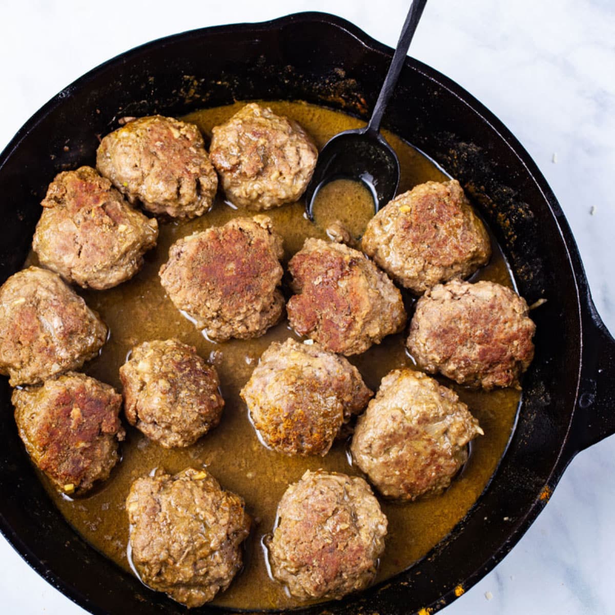 Black cast iron pan full of browned bison meatballs with pan sauce.