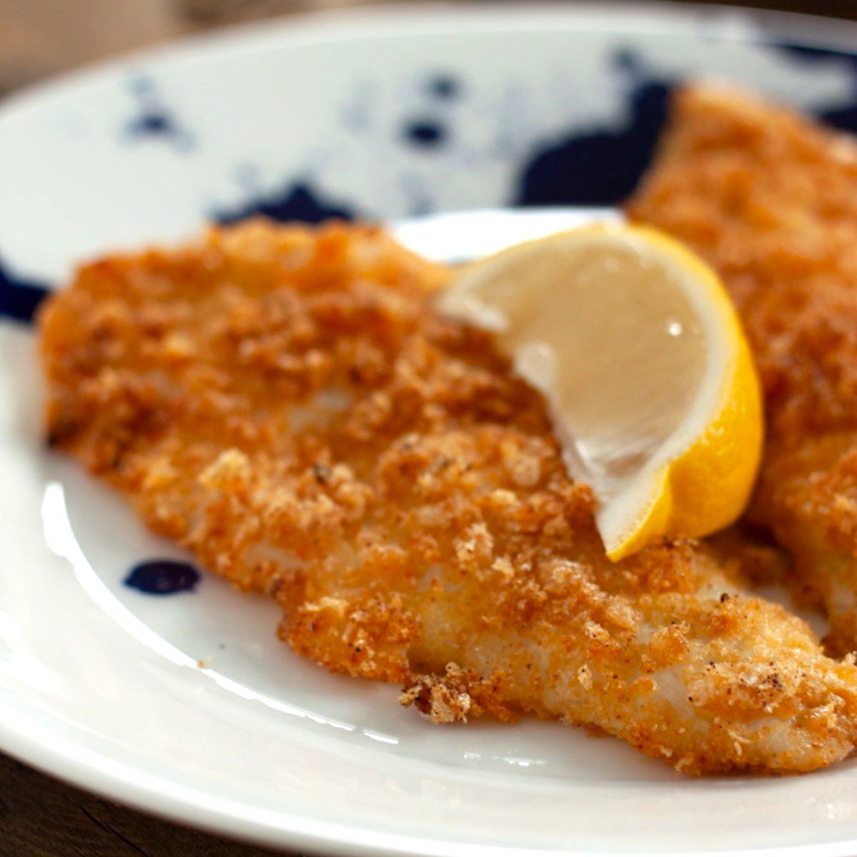 Crispy irregular shaped pieces of golden breaded fish pieces on a white and blue plate.