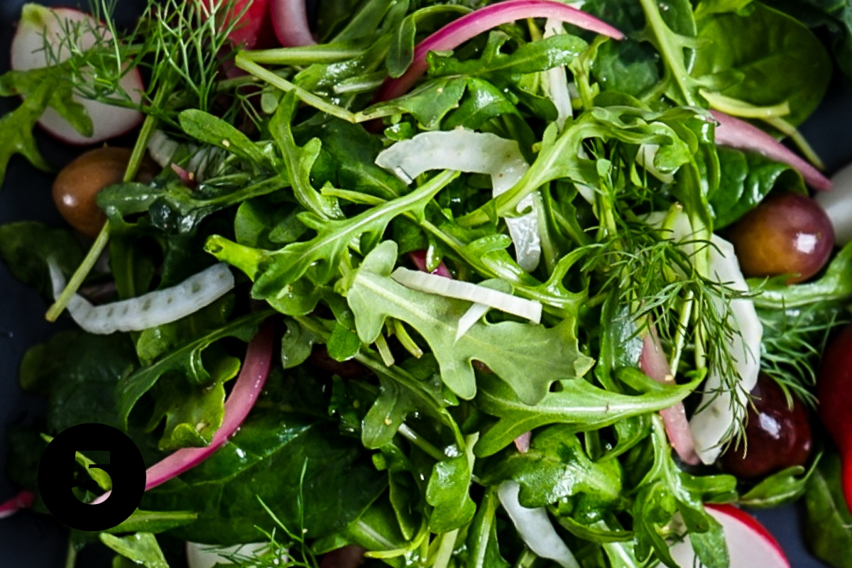 Simple green salad tossed with vinaigrette with slices of red onion, black olives, shaved fennel and radish in it.