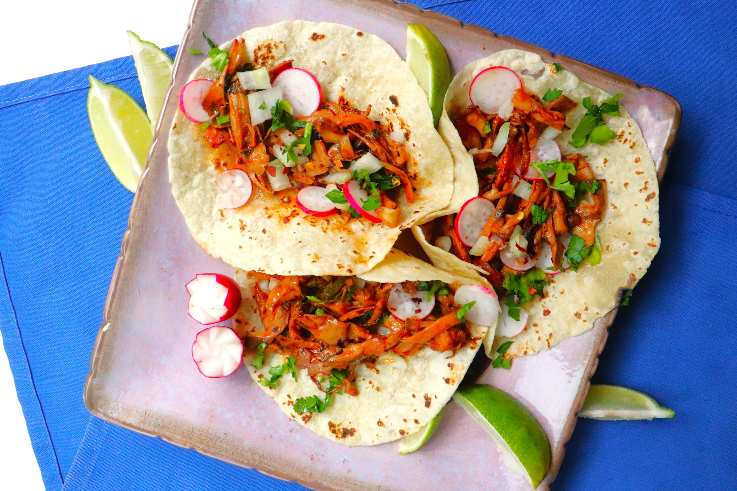 Bright orange filling inside flour tortillas with radishes, lime wedges and cilantro scattered around.