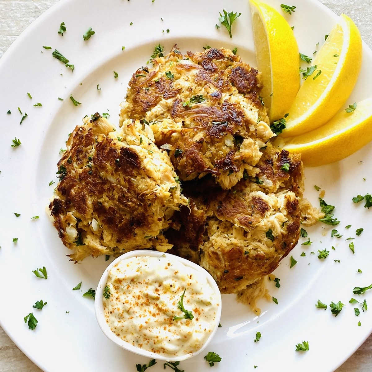 Small mushroom cakes on a white plate with a side of tartar sauce and 3 lemon wedges.