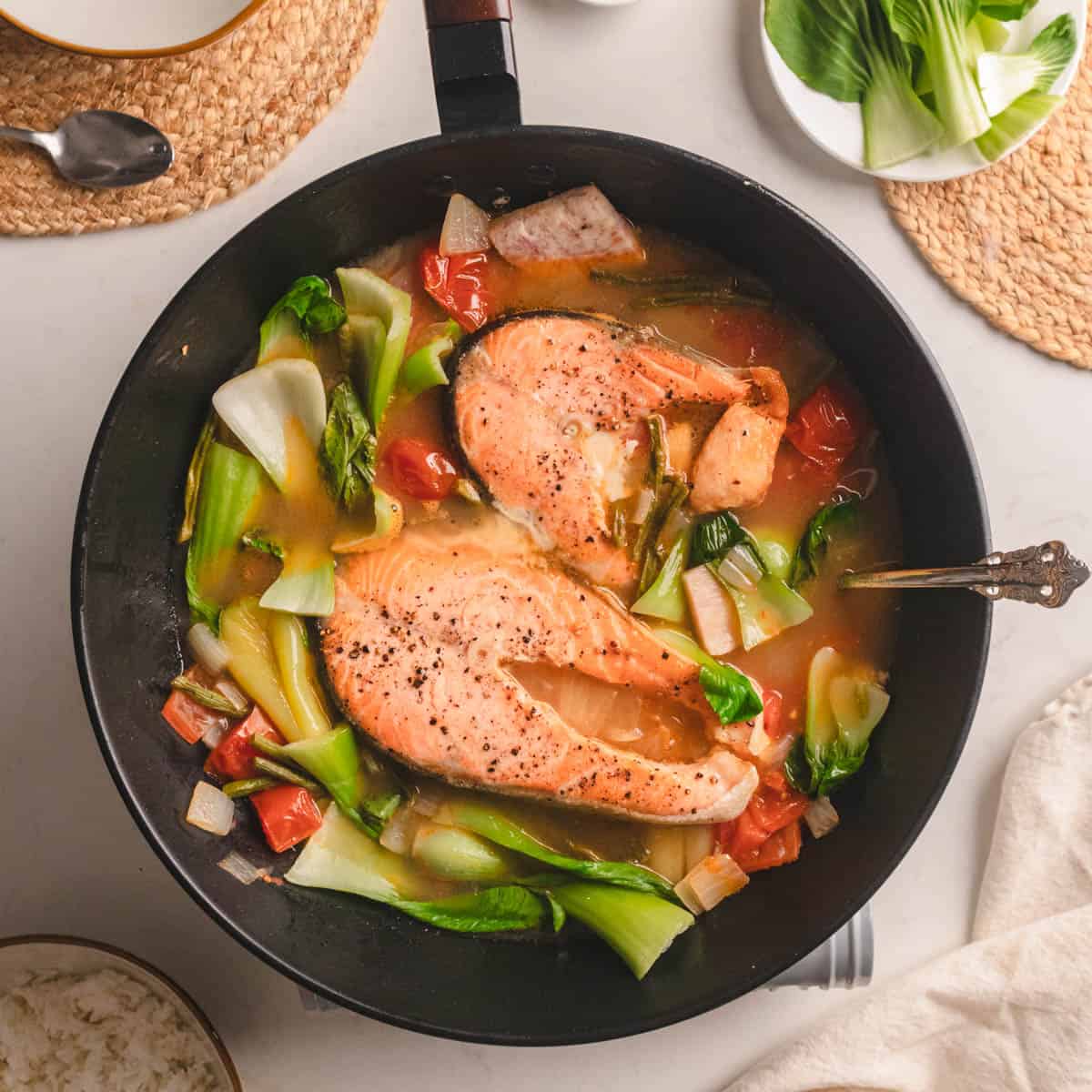 Black cast iron pan of green bok choy, broth and pink salmon steaks.