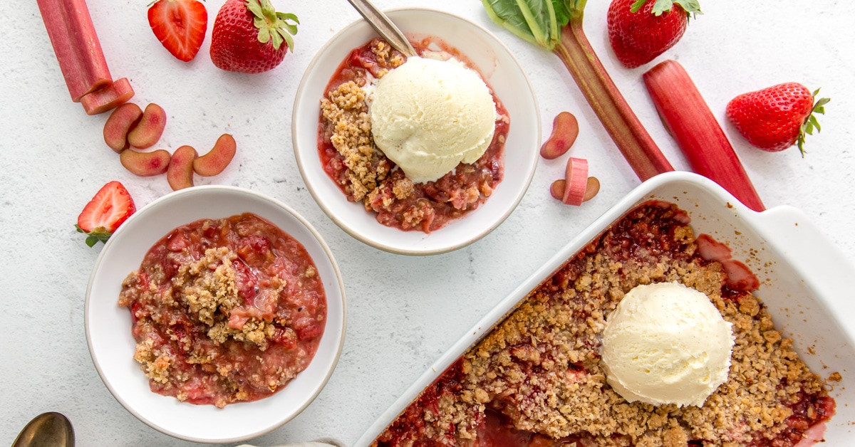 Bowls of oat topped pink fruit crisp with round scoops of white ice cream on top.