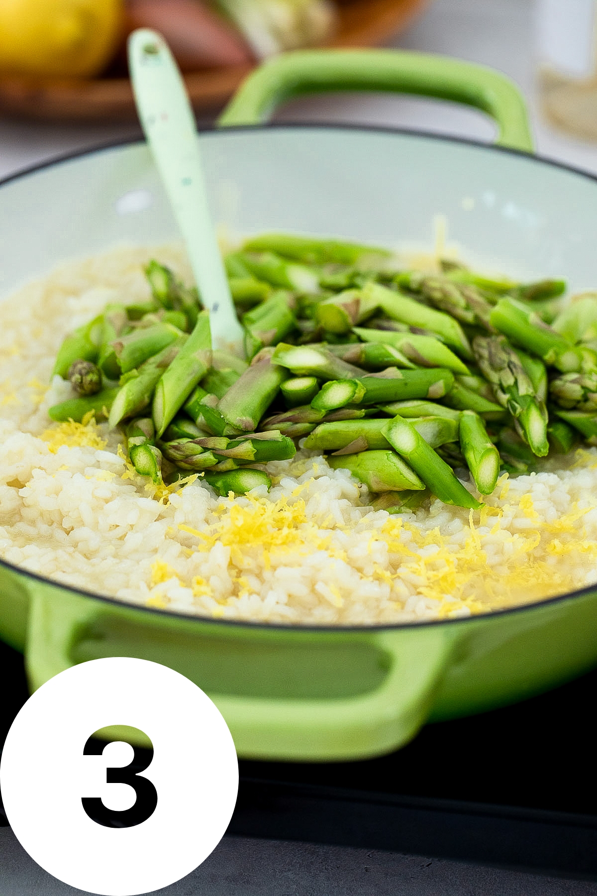 Pan of rice looks half cooked and has chopped asparagus and lemon zest on top.