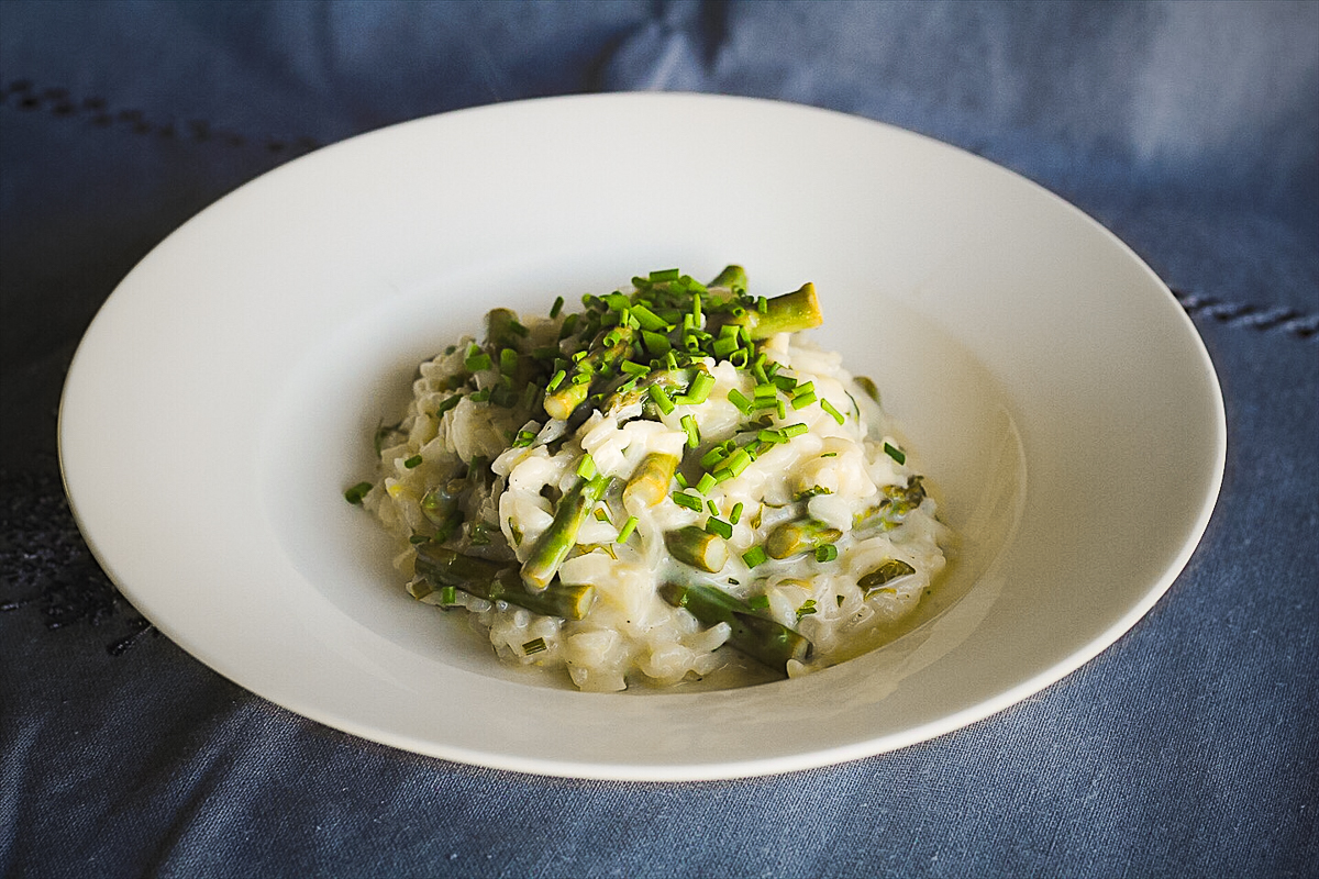 White bowl of creamy risotto with asparagus in it.