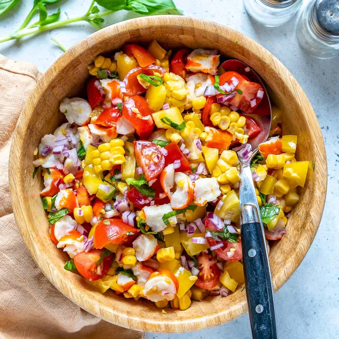 A bright salad of tomato, red pepper, corn, red onion and crab meat in a wooden bowl.
