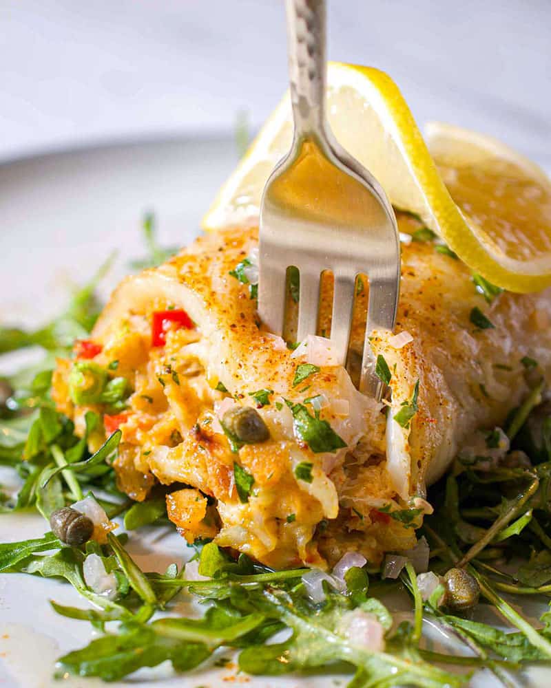 White fish wrapped around a creamy filling and sprinkled with paprika and capers. It's on a bed of arugula with a twist of lemon on top.